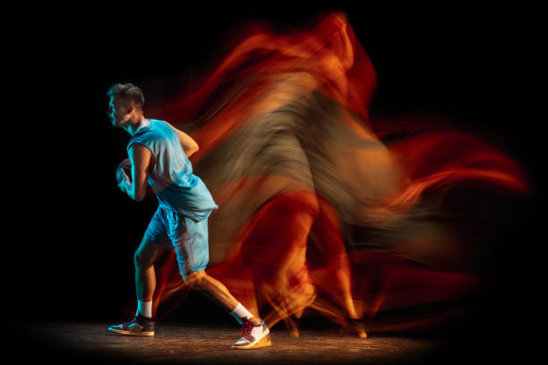 jeune joueur de basket-ball masculin caucasien jouant au basket-ball isolé sur un fond de studio sombre dans une lumière mélangée. concept de mode de vie sain, sport professionnel, passe-temps. - stroboscopic photos et images de collection