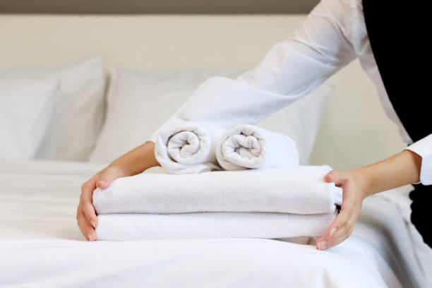 istock Room service housekeeper cleaning and making bed hotel room concept, woman hands putting stack of fresh white bath towels on bed sheet. 1327651492