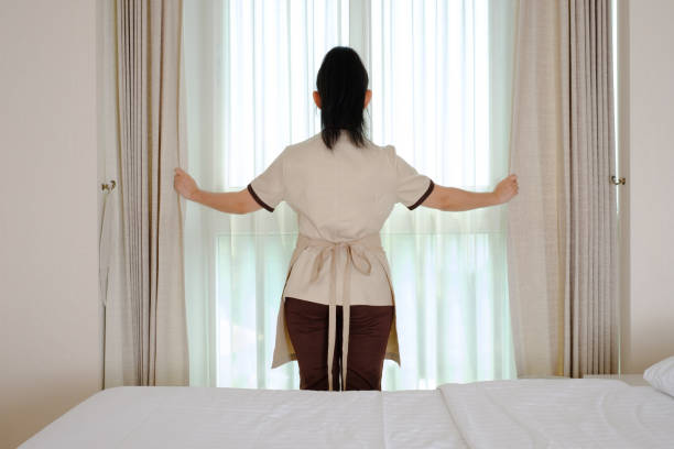 istock Young maid opening curtains in hotel room 1327652433