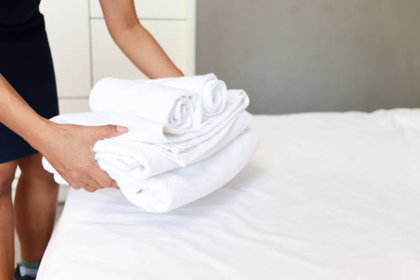 istock Room service housekeeper cleaning and making bed hotel room concept; woman hands putting stack of fresh white bath towels on bed sheet. 1327653364