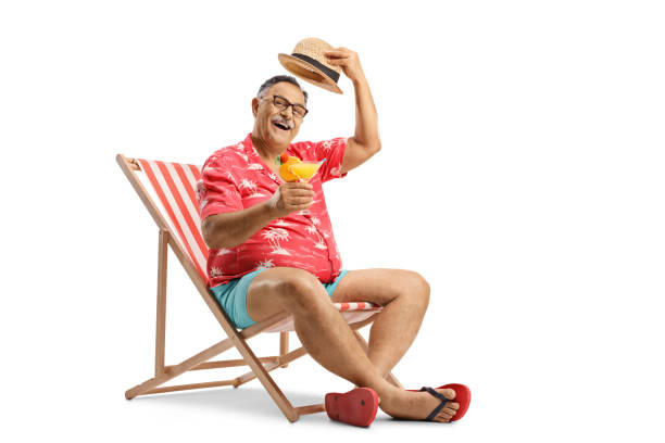 turista maduro brindando com um coquetel, sentado em uma cadeira de praia e cumprimentando com seu chapéu - espreguiçadeira - fotografias e filmes do acervo