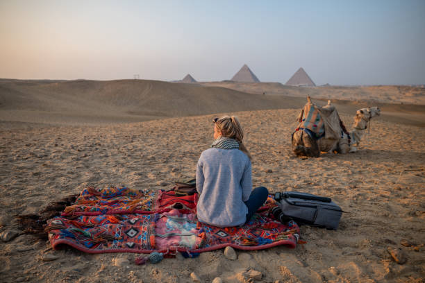 une femme regarde le coucher du soleil aux pyramides de gizeh, elle regarde à travers le désert du sahara - tourist egypt pyramid pyramid shape photos et images de collection
