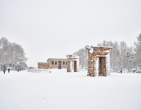 Citizens crossing the Cuartel de la Montana Park amid blizzard with the Temple of Debod in the background. Madrid, Spain.