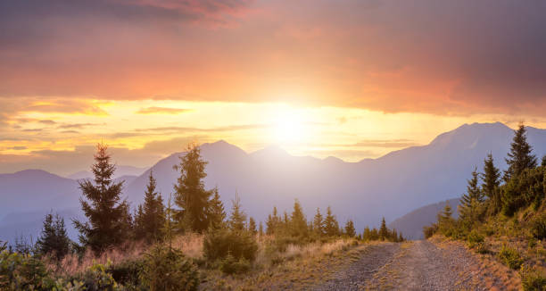 panorama des warmen sonnenuntergangs über hohen berghügeln mit einer schotterstraße davor. - mountain pass stock-fotos und bilder