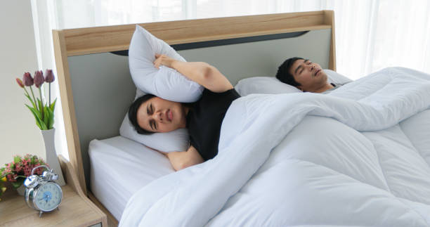 asiatische junge frau kann nicht schlafen, wie ihr mann neben ihr schnumst, frau schließt ohren mit einem kissen. - couple love snoring sleeping stock-fotos und bilder