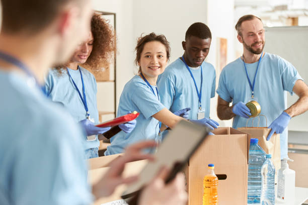 istock Cheerful diverse volunteers smiling while sorting foodstuff in cardboard boxes, working together on donation project. Focus on woman 1327672115