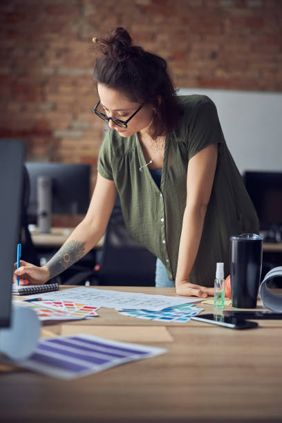 istock Interior designer or architect in casual wear with messy hairdo making notes while working on new project, standing in her office on a daytime 1327672159