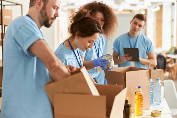 istock Diverse volunteers in protective gloves sorting, packing canned food in cardboard boxes, working together on donation project indoors 1327672179