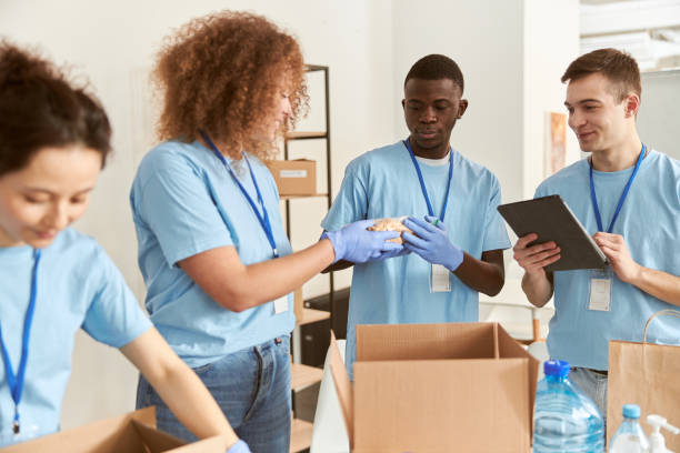 istock Diverse young volunteers in protective gloves sorting, packing foodstuff in cardboard boxes, working together on donation project indoors 1327672180