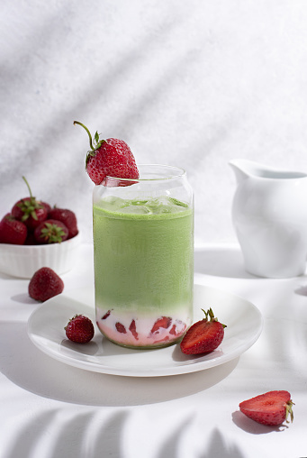Strawberry matcha latte with strawberries on a white plate with beautiful shadows from the leaves, close-up.