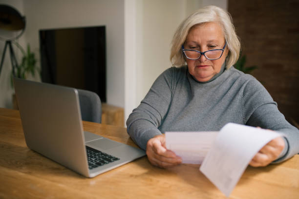 istock Senior woman is sitting at the table, looking at some papers. 1327677511
