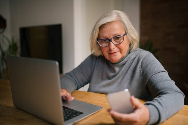 istock Senior blond woman using laptop and her phone. 1327677512