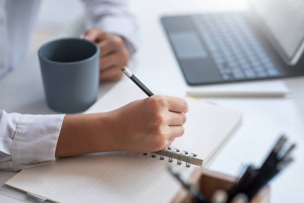 istock Business woman using a pencil to taking notes in his notebook. Along with your favorite coffee at the office.Business woman using a pencil to taking notes in his notebook. Along with your favorite coffee at the office. 1327677783
