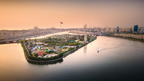 Flag island with large UAE flag pole and a ferris wheel at Emirate of Sharjah downtown in the United Arab Emirates at sunset