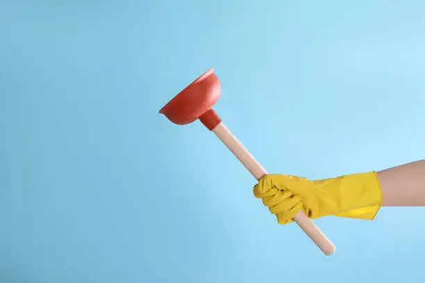 Woman holding plunger on turquoise background, closeup. Space for text