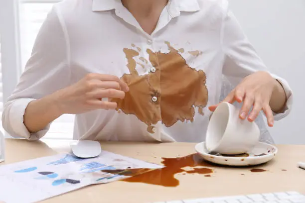 Woman in dirty shirt at wooden desk with coffee spill, closeup