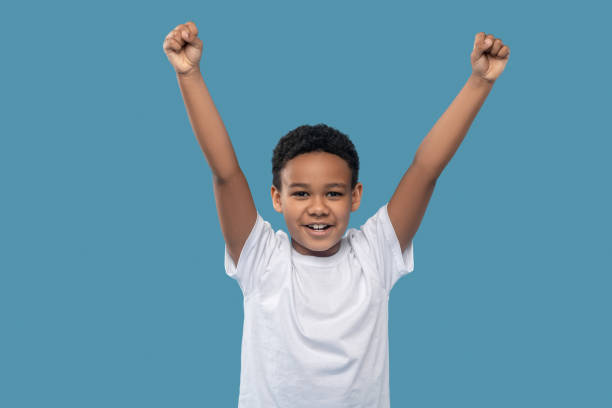 istock Dark skinned friendly boy with fists raised victoriously 1327680027