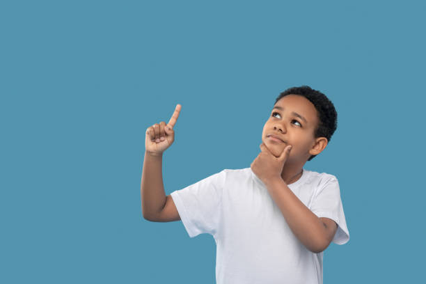 istock Pensive boy looking up pointing finger 1327680031