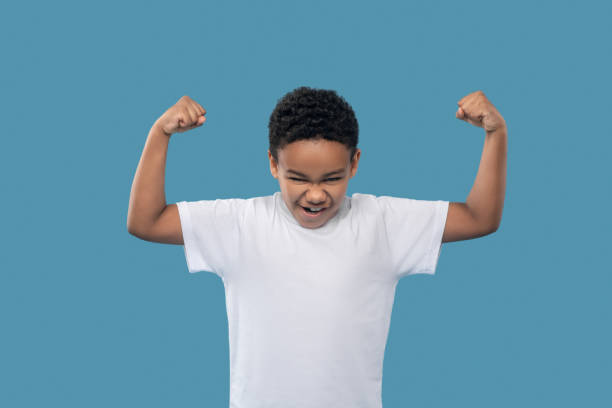 niño mostrando fuerza tensando los músculos del brazo - t shirt child white portrait fotografías e imágenes de stock