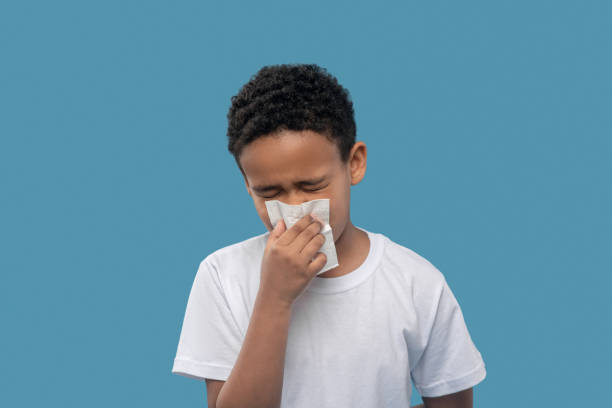 Boy with closed eyes and napkin near nose Runny nose. Dark skinned primary school age boy standing with closed eyes holding napkin near nose sneezing photos stock pictures, royalty-free photos & images