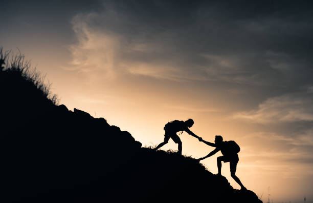 Man hiker helping his friend to climb the big mountain. stock photo