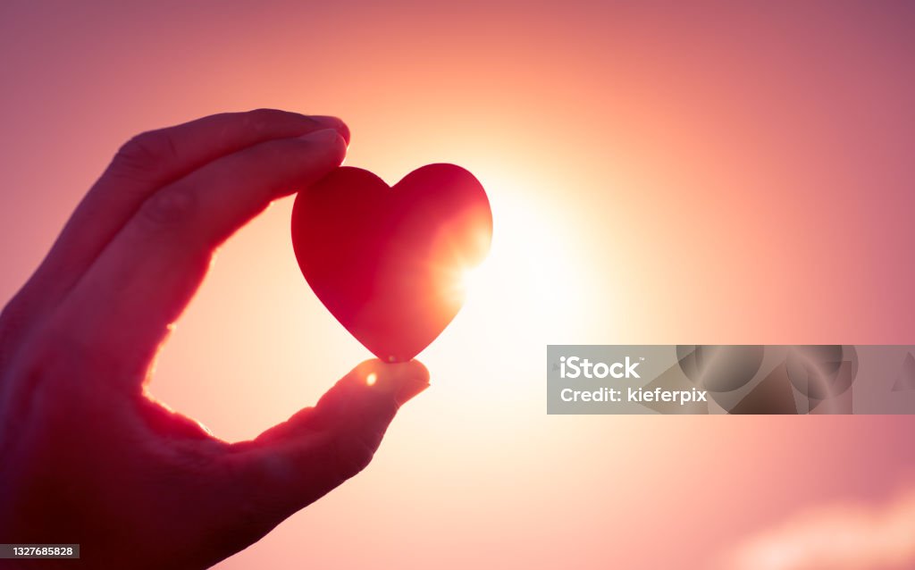 Hand holding heart against a sun Hand holding heart at sunset against a sun. Love - Emotion Stock Photo