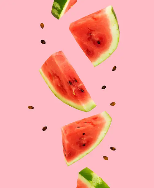 Photo of Floating, flying, levitating sliced fresh watermelon on pink background. Summer fruits, berries. Trendy, minimal Creative food. Concept of watermelon day-August 3.