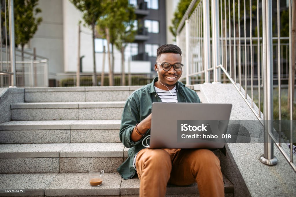 Using laptop for studying outdoor Young man sitting on the stairs in a front of the office building, working using laptop University Student Stock Photo