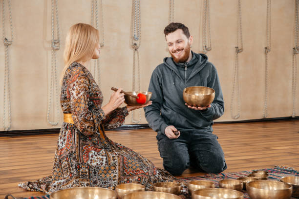 frau und mann spielen auf einer tibetischen klangschale für klangtherapie im yogastudio - third place audio stock-fotos und bilder