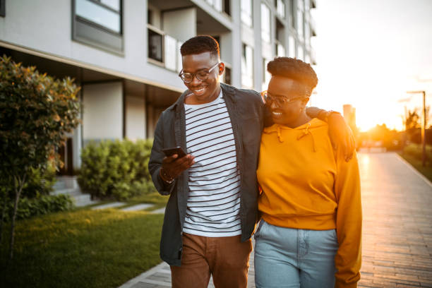 istock Embraced happy couple walking in sunset while looking at smart phone. 1327704533