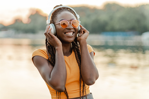 Photo of a young woman with headphones, she is listening to music and enjoying in sunset