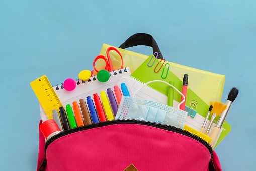 Back to school. Backpack for school or college with bright colorful school supplies on blue background. Stationery for school children's studies. Greeting card or banner for sale. close up