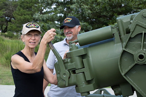 Vietnam Veteran male and Gulf War veteran female, with veterans caps at outdoor World War Two museum.