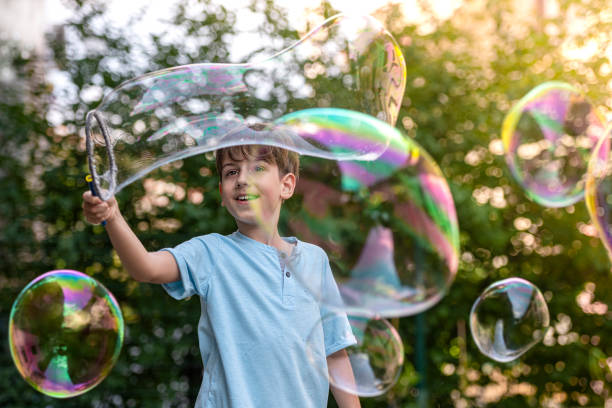 um garotinho está brincando no jardim dos fundos com uma varinha de bolha gigante. - bubble wand - fotografias e filmes do acervo