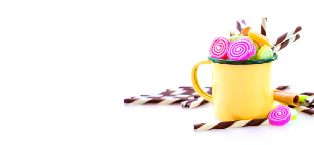 Stock photo showing close-up view of mini, edible cake decorations shaped like a gingerbread man, a snowflake and a Christmas tree sitting on whipped cream topping a red cup and saucer with overflowing, dripping, hot chocolate.