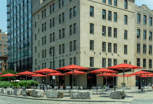 Landscape view of a public square lined with red umbrellas in the trendy Meatpacking District at the intersection of Gansevoort St, 9th Ave, and Little West 12th St. New York, NY - USA - July 6, 2021: Landscape view of a public square lined with red umbrellas in the trendy Meatpacking District at the intersection of Gansevoort St, 9th Ave, and Little West 12th St. logan west stock pictures, royalty-free photos & images