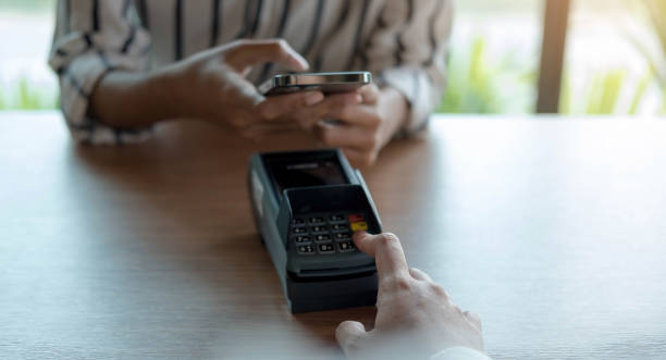 istock Woman paying bill through smartphone using NFC technology in a coffee. customer paying through mobile phone using contactless technology. Closeup hands of mobile payment at a coffee shop 1327734116