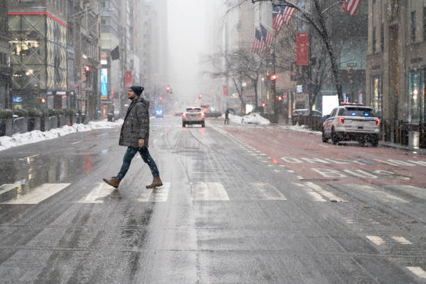 jeune homme, touriste, traversant la 5e avenue à manhattan sous une forte chute de neige - overcast day new york city manhattan photos et images de collection