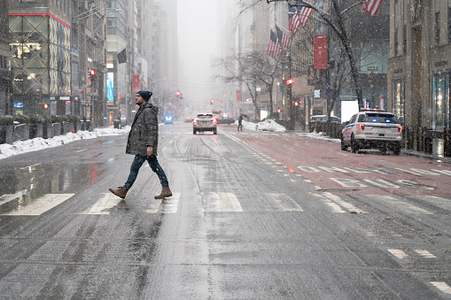 A man crossing the street in a big city under a snowfall during the winter storm.