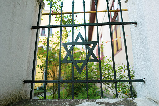 Close up color image depicting a Jewish Star of David decoration on an iron gate outside a synagogue. Focus is on the star in the centre of the frame, with the rest attractively blurred out of focus. Room for copy space.