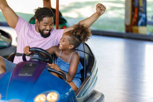 Father and Daughter of African-American Ethnicity are Spending a Wonderful Day While Driving in Bumper Car in Luna Park.