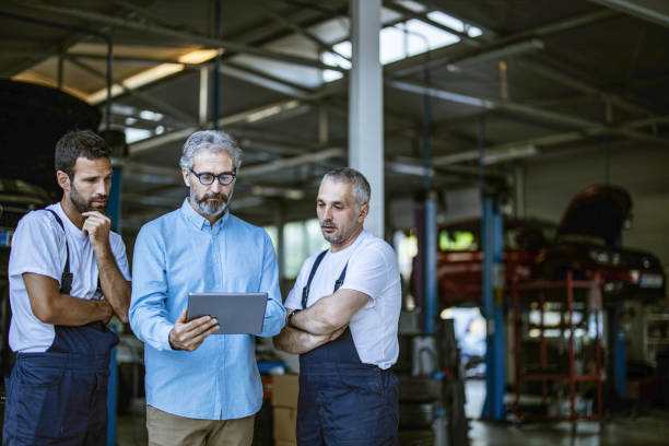 istock Mature manager using digital tablet with mechanics in a repair shop. 1327756033