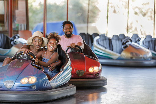 Mother and Daughter of African-American Ethnicity are Spending a Wonderful Day While Driving in Bumper Car in Luna Park.