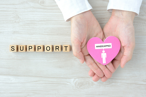 Human's hands holding heart object with handicapped person pictogram and wooden blocks with support word
