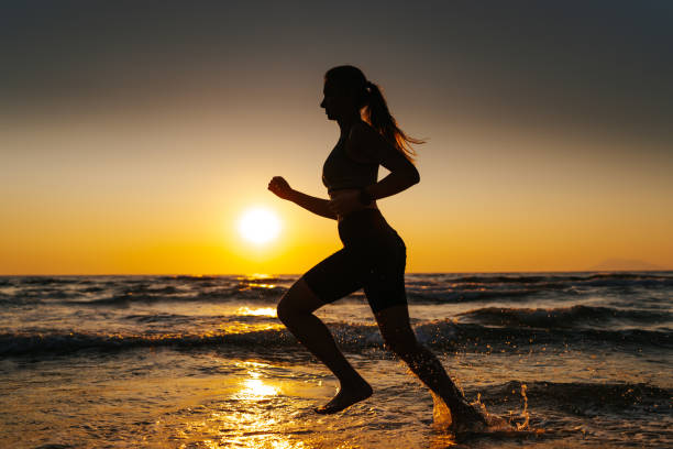 istock Young woman running on the beach at sunset 1327756982