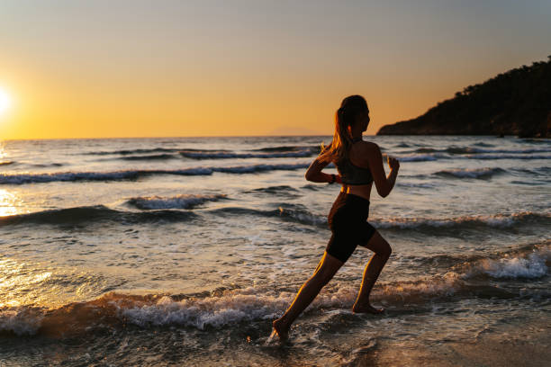 istock Young woman running on the beach at sunset 1327757609