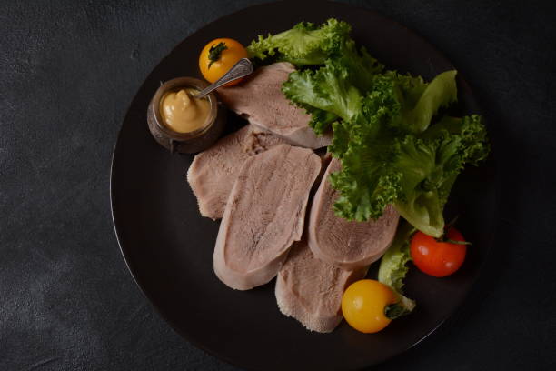 sliced beef tongue slices on a platter with lettuce leaves, cherry tomatoes and dijon mustard on a black background - smoked tongue imagens e fotografias de stock