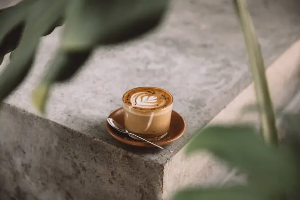 Photo of Glass of cappuccino with latte art on saucer and with spoon on the concreet background