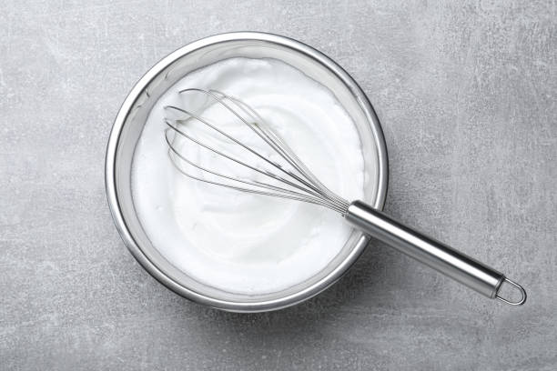 istock Whipped egg whites with balloon whisk on grey table, top view 1327762136
