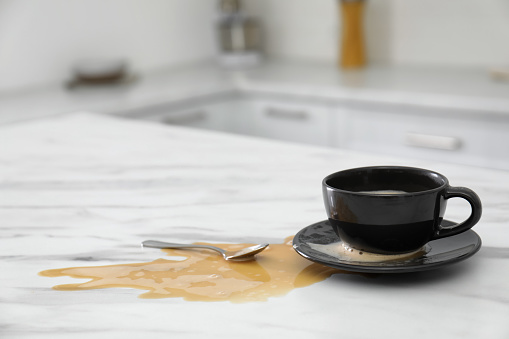 Cup and spilled coffee on white marble table in kitchen, space for text